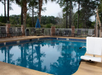 Outdoor swimming pool surrounded by trees and lounge chairs, with a lift chair on the side and an umbrella in the background.