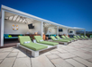 Poolside cabanas with green lounge chairs and white towels under a clear blue sky.