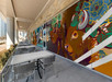 Outdoor seating area with metal tables and chairs beside a colorful mural featuring bison and floral elements.