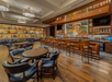 A stylish bar with wooden floors, leather chairs, and a stocked bar. Shelves with decor are in the background, and a large cowboy mural is above the bar counter.