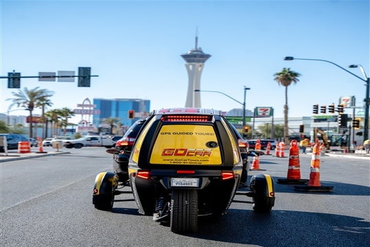The back of a yellow GoCar stopped in traffic with the company's contact info and logo on the back panel in Las Vegas.