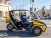 A man and woman in a two-seater doorless yellow GoCar smiling and having a good time on a sunny day in Las Vegas.