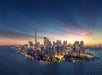 Wide shot of the island of Manhattan at dusk with the city glowing with lights and a pastel sunset in the background.