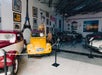 Classic cars are displayed indoors alongside wall art featuring Paris and Italy-themed decorations, including an Eiffel Tower mural and framed pictures.