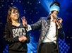 A magician with a blindfold holds a microphone and gestures beside a smiling woman wearing glasses and a shirt that says "DON'T SWEAT MY".