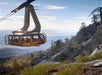 A tramcar full of people in the air in the mountains with the sun shining on it exterior at Palm Springs Aerial Tramway.