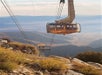 A yellow tramcar with people in it in the air with the mountains in the distance it at Palm Springs Aerial Tramway.