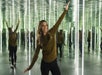 A woman posing with her arms out in a room full of mirrors showing her reflection.