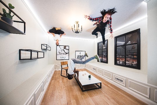 The Reverse Room of the Paradox Museum with three people who appear to be floating around a white room with windows on the right.