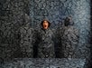 A woman wearing a shocked expression stands alongside two others, all clad in full-body camouflage coats designed to match the room's exact pattern and color, creating a mesmerizing visual illusion at Paradox Museum Las Vegas, NV
