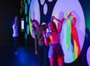 Two women strike a pose, forming a hand heart gesture together, as colored shadows of them cast onto their backs at Paradox Museum Las Vegas, NV
