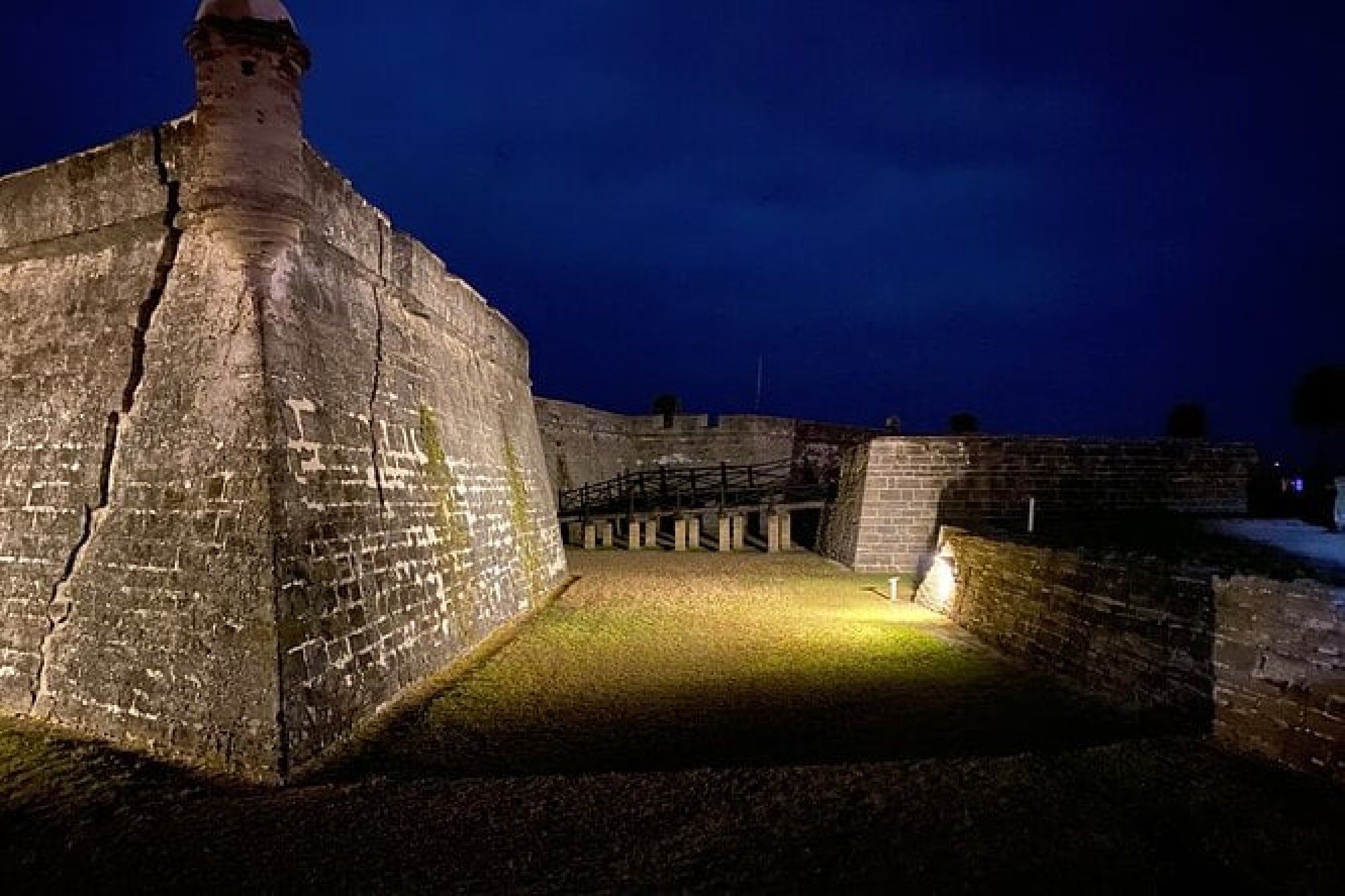 Stone fortress walls illuminated at night, with a dark blue sky in the background.