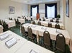 A conference room with rows of empty tables and chairs, each table set with paper materials. A podium is in front of windows with curtains.