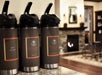 Three coffee dispensers labeled hot water, decaf, and gourmet are placed on a counter near a lit fireplace in a cozy room.