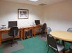 Small office with two workstations featuring computers and printers, a round table with chairs, and a framed picture on the wall.