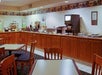 Empty hotel breakfast area with wooden tables and chairs, a counter with a beverage dispenser, food trays, and a toaster, decorated with rooster-themed wallpaper border.