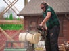 A man wearing safety gear operates a chainsaw to cut through a log, with wood chips flying, during a lumberjack competition.
