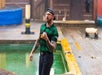 A lumberjack in a green plaid shirt and a hat in front of a pool of green water yelling with his fist halfway up.