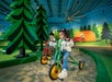 Two children ride tricycles on a path surrounded by painted trees and a tent in a play area.