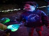 A child wearing a "Phoenix Zoo Arizona" hoodie. They are smiling and holding a bubble-blowing toy with colorful lights at night.