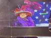 Kyle Martin wearing a purple boa, sun glasses, and large colorfully decorated hat while singing and playing the piano.