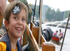 Smiling child wearing a pirate eye patch stands on a wooden boat, with people in another boat spraying water in the background.