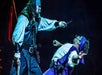 Two performers in pirate costumes engage in a staged sword fight on a dimly lit stage.