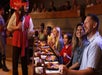 A server dressed as a pirate pours drinks for a group of people sitting at a table with plates of food, smiling and enjoying a themed dining experience.