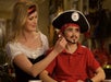 An adult helps a child dressed in a pirate hat and red shirt apply face paint for a pirate costume.