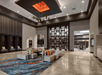 Spacious lobby with modern seating, decorative rug, and a large geometric ceiling light. Wood accents and shelving create a contemporary atmosphere.