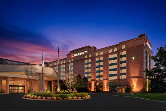 A large, illuminated hotel building labeled "Marriott" at dusk, surrounded by trees and landscaped grounds.