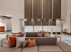 Hotel lobby with modern decor featuring brown couches adorned with gray and orange pillows, potted plants on tables, and a wooden slatted wall behind a white reception desk.