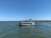 A person stands on a blue and white pontoon boat floating on calm water under a clear blue sky.