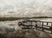 A wooden dock with a covered boat is reflected in the calm, still water of a lake under a cloudy sky.