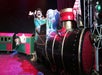A person in a colorful costume drives a small train with three cars, each carrying a dog, on a stage with theatrical lighting.