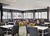 The M Club's modern dining room with several windows, gray booth seating along the outer wall, and white table with gray chairs.