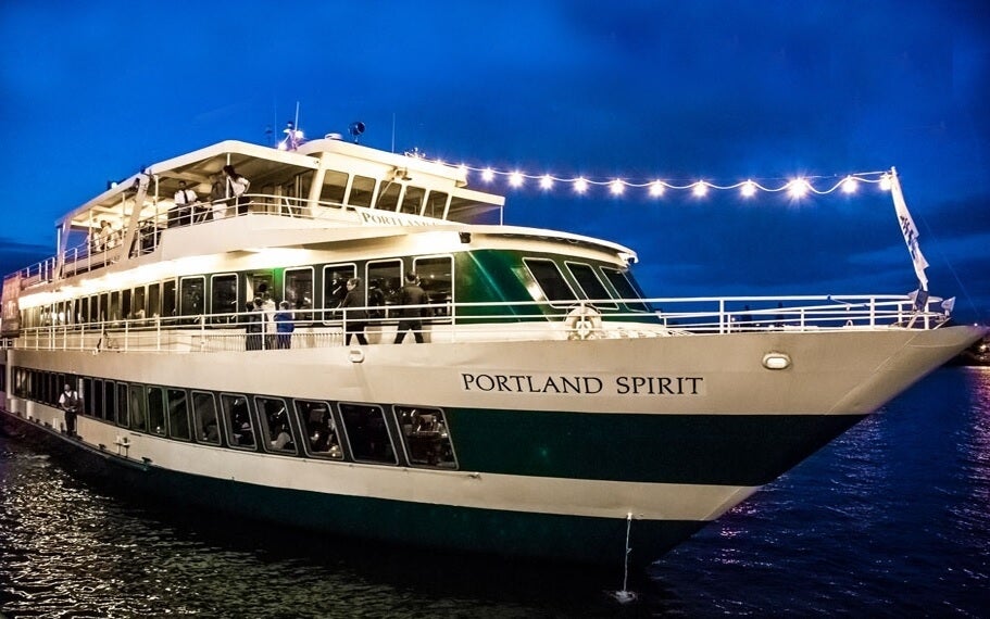 A large cruise ship named "Portland Spirit" illuminated by string lights docked at night.