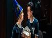 Two people in black shirts labeled "Potted 2" perform; one wears a blue wizard hat with stars and holds an open book, both look at each other with surprised expressions.