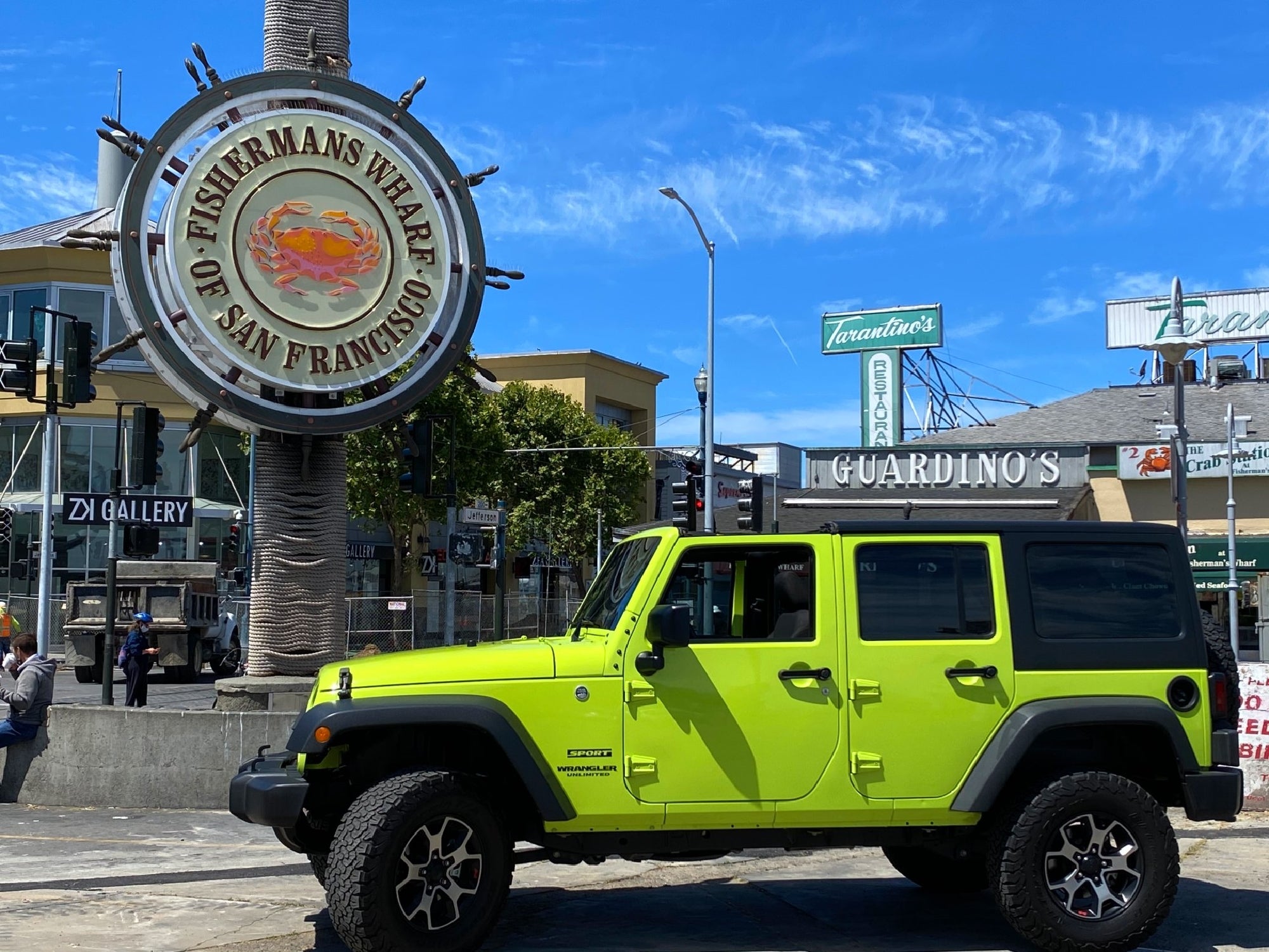 A bright green Jeep is parked near the Fisherman's Wharf sign in San Francisco under a clear blue sky.