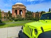 A bright green Jeep is parked in front of the Palace of Fine Arts, with greenery and a pond visible in the background.