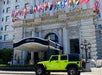 A bright green Jeep is parked in front of the Fairmont hotel entrance, with multiple international flags displayed above the building’s entrance.