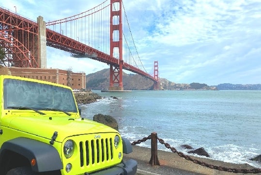 A bright green Jeep parked near the water with the Golden Gate Bridge in the background on a sunny day in San Francisco.