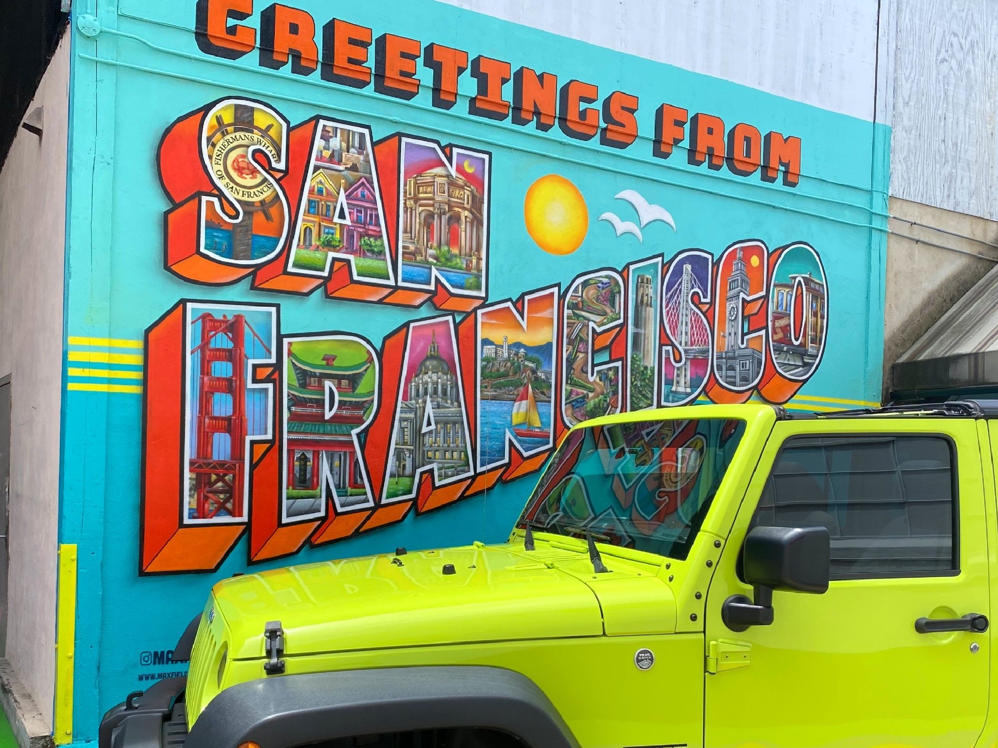 A bright yellow Jeep parked in front of a colorful mural that reads “Greetings from San Francisco” with city landmarks illustrated inside the letters.