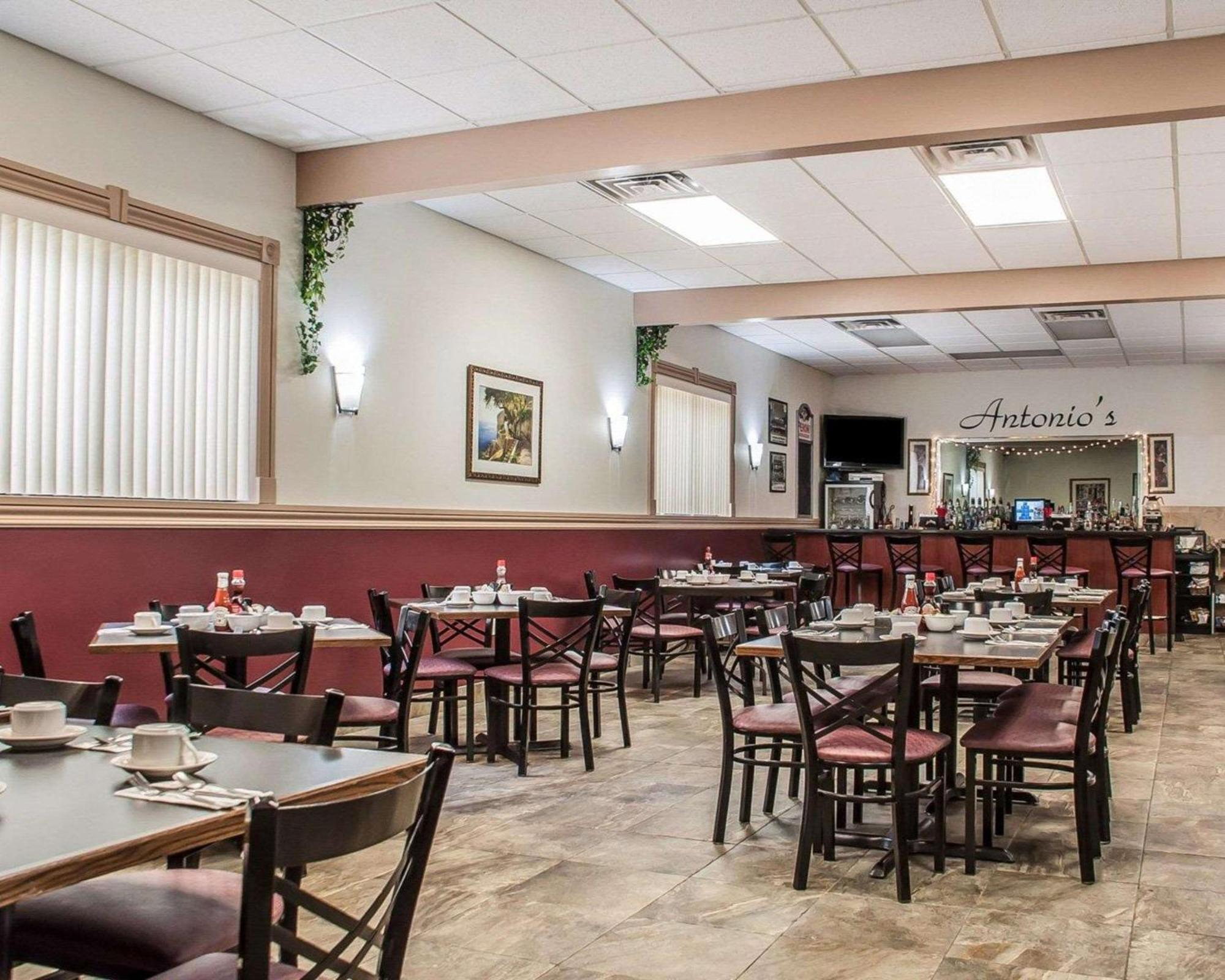 Dining area of a restaurant with neatly arranged tables and chairs, place settings, wall art, and a bar area in the background labeled "Antonio's.