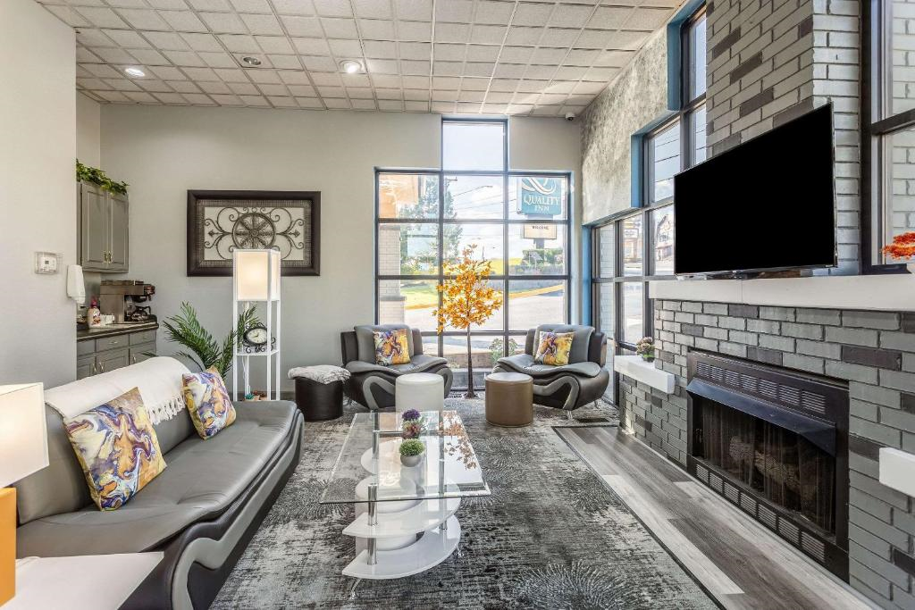 Cozy modern living room with gray sofas, colorful cushions, a glass coffee table, and a brick fireplace. Large windows let in natural light.