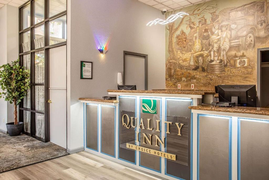 Reception desk at Quality Inn with a mural on the wall and a small potted plant to the left.
