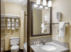 Hotel bathroom with a granite countertop, sink, mirror, and wall-mounted hairdryer. There is a toilet, shower, towel rack, and overhead lighting.