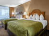 A guest room with two Queen beds and lamps on each side at Quality Inn Kennedy Space Center, Florida.