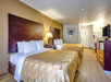 Hotel room with two double beds, a nightstand with a lamp, a TV on a dresser, a microwave, a fridge, and a picture on the wall. Wood flooring and neutral-colored bedding.