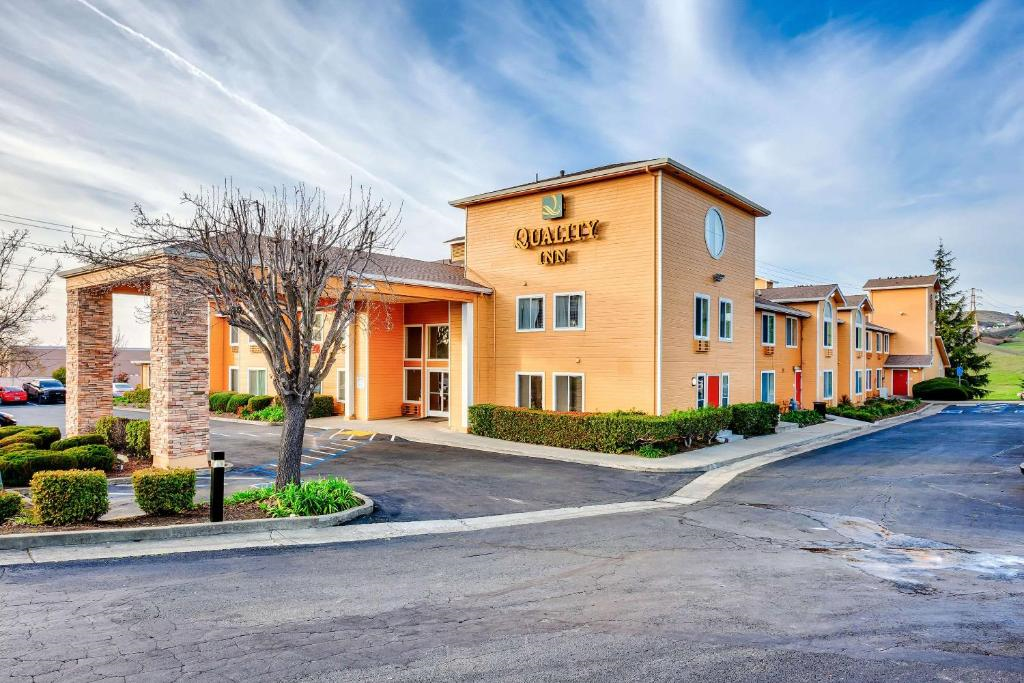 Exterior view of the Quality Inn hotel, featuring a two-story building with tan siding, a columned entrance, and a parking area in front.